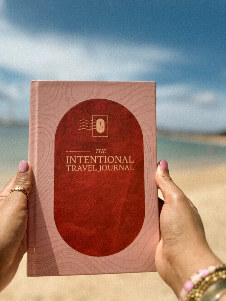The Intentional Travel Journal held up beside the sea