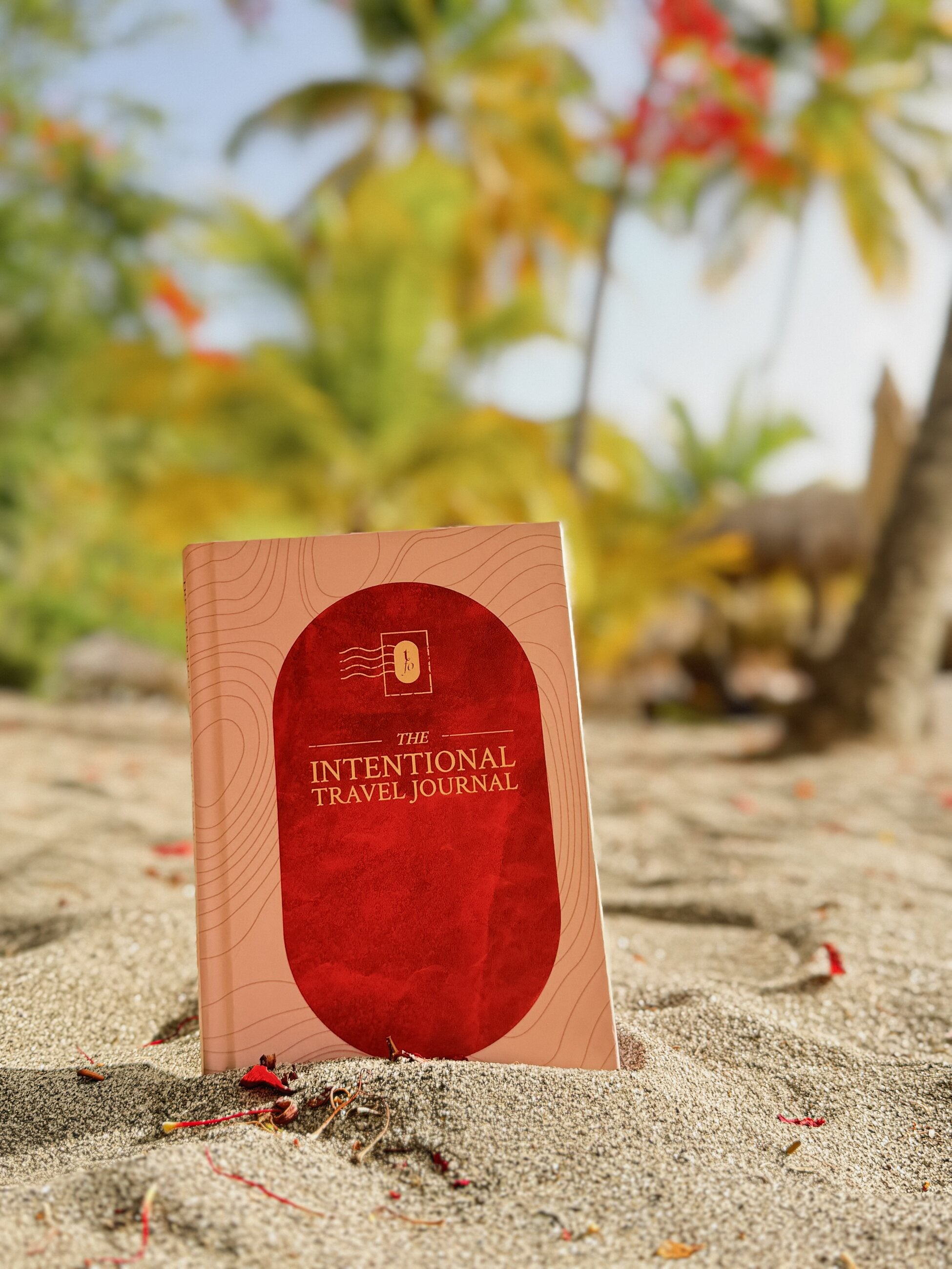 The Intentional Travel Journal standing on sand beneath tropical foliage