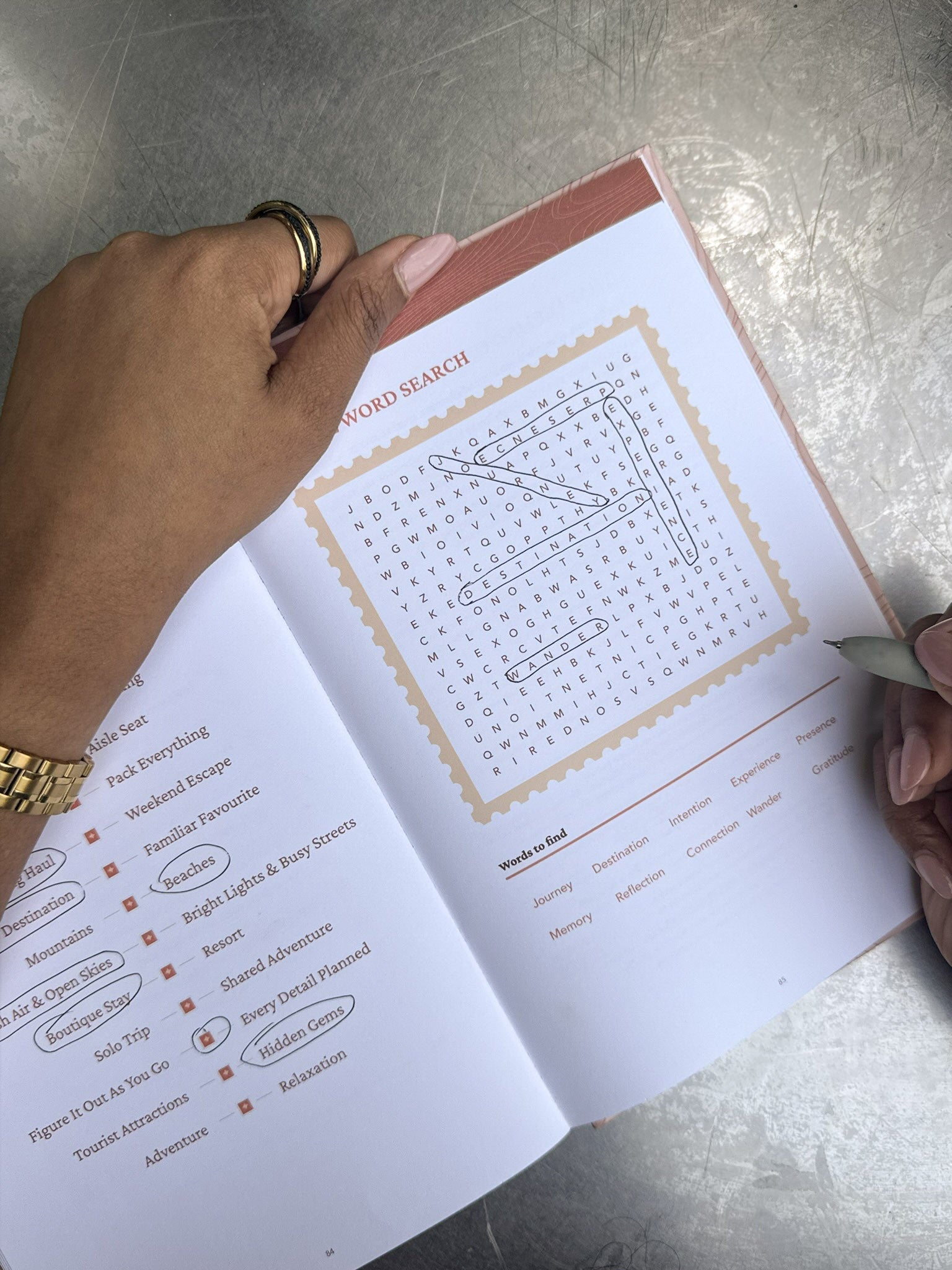Hands use the journal’s travel word search and activity page.
